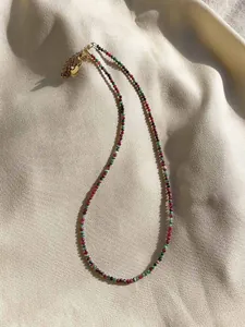 Close-up of thin red and green gemstone beaded necklace on silk with gold heart pendant