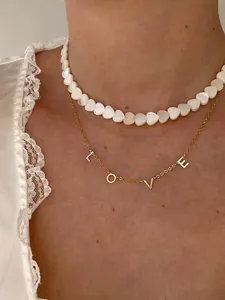 Detail of beaded shell heart choker with 18k gold plated LOVE letter charms on a model