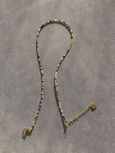 Detail of beaded necklace with gold heart pendant and lobster clasp on grey fabric