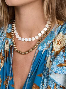 Detail of layered gold beaded necklace with white shell heart charms on a female model