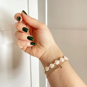 Detail of layered handmade shell heart beaded bracelet and gold chain on wrist