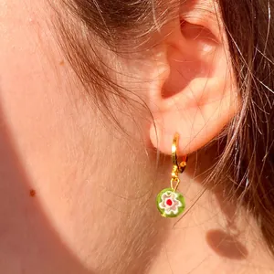Primer plano de un pendiente de aro dorado con colgante de cristal millefiori verde en modelo