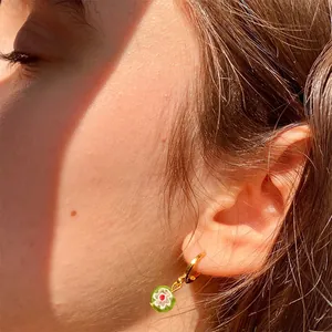 Pendiente de aro dorado con colgante de flor de cristal verde puesto en la oreja