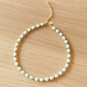 Freshwater pearl necklace with green beads and gold lobster clasp on wood background