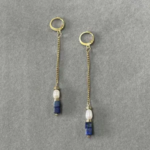 Dettaglio di orecchini a pendente con perle naturali e pietre blu su catena dorata
