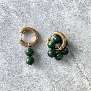 Dettaglio ravvicinato di orecchini a cerchio placcati oro 18k con pietre verdi
