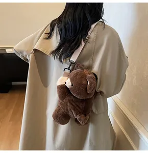 Brown fluffy teddy bear plush crossbody bag with a wide cream shoulder strap shown on model