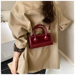 Detail of burgundy glossy handbag with cylindrical handle and detachable shoulder strap