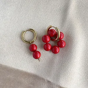 Dettaglio di orecchini placcati oro 18 carati con perline rosse su sfondo di seta