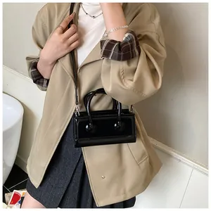 Fashionable black glossy patent leather crossbody bag styled with a beige trench coat