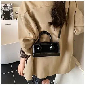Detail of a black patent leather rectangular handbag styled on a model's shoulder