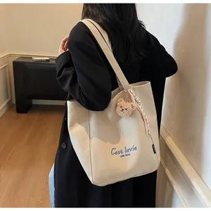 Détail d'un cabas en toile crème avec texte bleu et pendentif ours en peluche