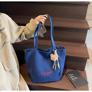 Détail du sac cabas en toile bleue avec broderie rouge et un petit ours en peluche