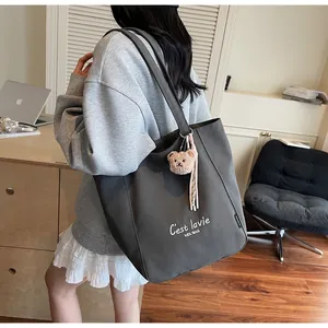 Détail du grand sac cabas en toile gris foncé avec lettrage blanc et breloque ours en peluche
