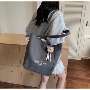 Détail du cabas en toile gris foncé avec lettrage blanc et breloque ours en peluche