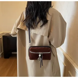 Macro shot of dark brown suede crossbody bag with metal zipper and robot pendant charm