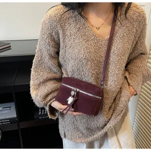 Detail of burgundy suede crossbody bag with silver zipper and unique metal pendants