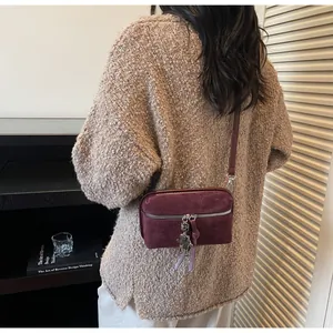 Detail of burgundy suede-texture crossbody bag with a unique silver robot charm