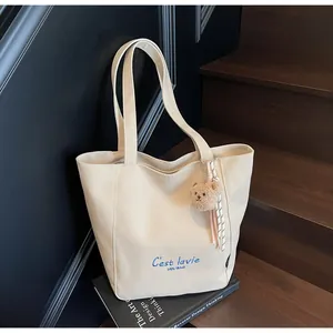 Détail du cabas en toile beige avec broderie bleue et breloque petit ourson