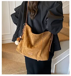 Brown faux suede hobo bag with contrast stitching and decorative plush pompom charms
