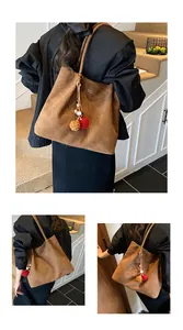 Close-up of brown suede tote bag featuring a decorative pompom tassel and gold lettering
