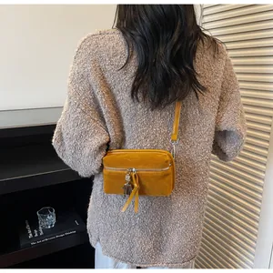 Detail of a mustard yellow suede crossbody bag with a unique robot charm on a model