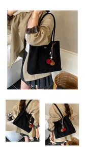 Close-up of black tote bag with decorative dual-color fur ball charms and printed text