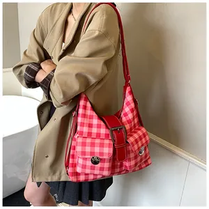Detailed view of red checkered shoulder bag with dual front pockets and silver buckles