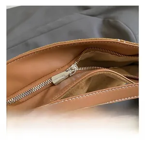Detail shot of a brown leather shoulder bag with a silver metal zipper and white stitching