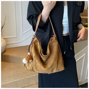 Detail of caramel brown suede tote bag with decorative pompom worn on shoulder