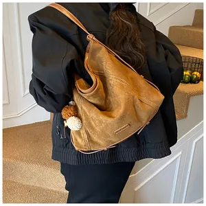 Detail of caramel brown suede hobo bag with white stitching and plush pompom charm