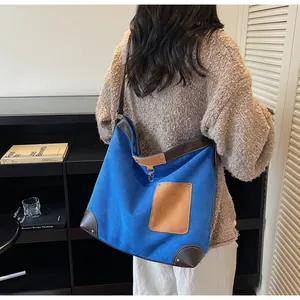 Detail of blue canvas tote bag with brown leather trim and metal rivets worn on shoulder