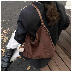 Detail of large brown suede tote bag with white contrast stitching and plush keychain