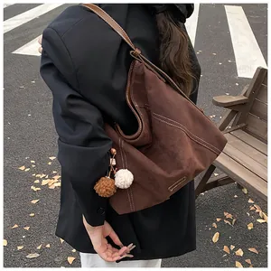 Detail of dark brown tote bag with white contrast stitching and soft pompom charm