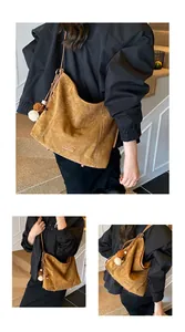 Macro view of brown suede hobo bag featuring white contrast stitching and plush charm decoration