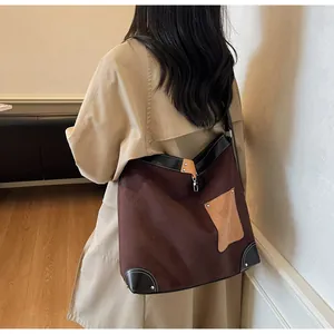 Detail of a large suede tote bag with brown textures, metal rivets, and contrast stitching