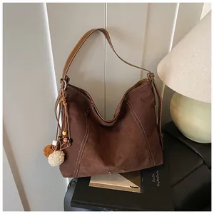 Detail of dark brown suede tote bag featuring white contrast stitching and plush ball charm