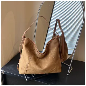Detail of soft brown suede hobo bag with side drawstring on dark wooden desk