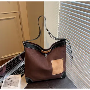 Detail of suede tote bag with contrast pocket and adjustable leather straps on a desk