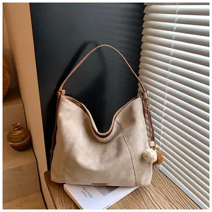 Detail view of beige suede tote bag with brown leather straps and plush pompom charm