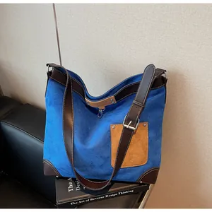 Detail of blue suede tote bag showing brown leather trim and protective metal feet