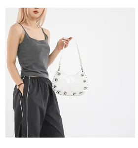 Close-up of white patent leather crescent bag with silver stud and rivet accents