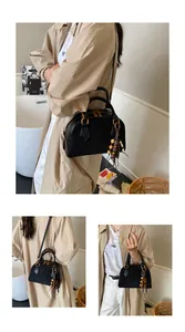Detail of black shell bag with matte leather texture and decorative wood bead tassel