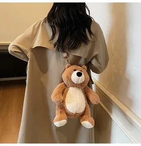 Brown plush bear crossbody bag with adjustable leather strap shown on a khaki trench coat