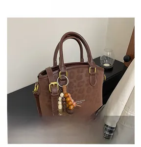 Détail d'un sac à bandoulière marron foncé avec texture léopard et breloque en perles