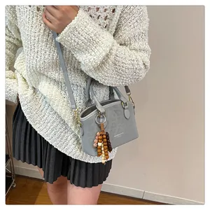 Détail du sac à main gris avec texture animale, ferrures dorées et gland en perles de bois