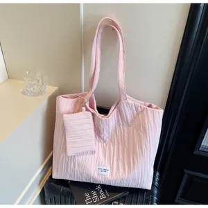 Détail de sac cabas en toile plissée rose avec mini pochette sur une valise noire
