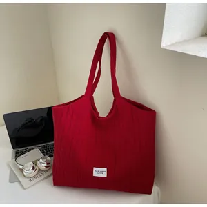 Détail du sac cabas rouge en toile texturée avec étiquette et décor de bureau créatif