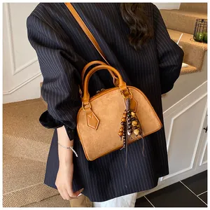 Close-up of brown suede shell bag featuring vintage wooden bead charm and dual handles