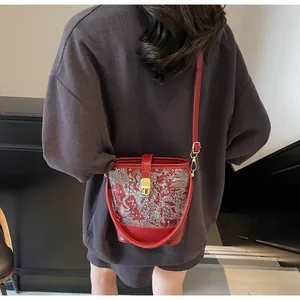 Detailed embroidery on a red Chinese bucket bag with golden buckle and crossbody strap
